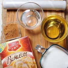 1 1/3 tazas de agua caliente papel encerado al gusto 1/4 taza de canela en polvo 2 tazas de azúcar blanca aceite de canola al gusto 500 gramos de harina para buñuelos Tres Estrellas