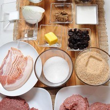 1 1/2 cucharitas de sal 500 gramos de carne molida de res 500 gramos de carne molida de puerco 1 cucharada de mostaza dijón 1/4 taza de uva pasa 1/4 taza de almendras picadas 1/4 pieza de cebolla blanca 6 rebanadas de tocino 1/4 taza de leche de vaca 2 piezas de huevo pan molido al gusto 1/2 cucharita de pimienta negra molida 1 trozo de mantequilla papel aluminio al gusto 3 piezas de huevo Ingredientes para salsa: 2 tazas de mora azul 1/2 taza de azúcar blanca