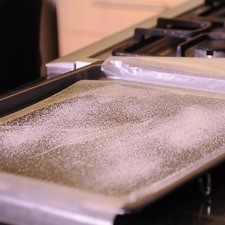 En una charola de horno por la parte de atrás rociar aceite y colocar un papel encerado, esparcir un poco de azúcar,