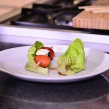 Preparar las brochetas, ensartar primero la mitad de un jitomate con la parte gorda hacia arriba, un trozo de queso feta y la aceituna, repetir hasta llenar la brocheta.