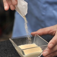 Para preparar la gelatina de leche tomar ¼ de taza de leche fría y espolvorear un sobre de grenetina natural de 7 gramos sobre ella en forma de lluvia. Mezclar ligeramente con un tendedor y dejar reposar 5 minutos para que se hidrate la grenetina.