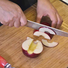 Cortar las manzanas en dos partes. Colocar la mitad de la manzana sobre la tabla de picar y cortar con el cuchillo en rebanas delgaditas hasta terminar de rebanar las manzanas.