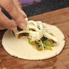 Desmenuzar el queso, colocar un poco de queso y una cucharada de flor de calabaza en cada tortilla. Doblar por la mitad y calentar sobre el comal por un lado y luego por el otro hasta que el queso se derrita.