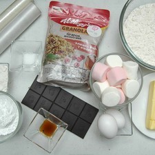 Ingredientes para receta 350 gramos de harina de trigo 150 gramos de mantequilla sin sal 150 gramos de granola de keloggs 1 pieza de huevo 1 pieza de yema de huevo 1 cucharada de esencia de vainilla 1 pizca de sal 15 piezas de malvaviscos 10 piezas de chocolate semi amargo para repostería harina de trigo al gusto papel plástico adherente al gusto papel encerado al gusto 100 gramos de azúcar glass (pulverizada)