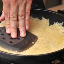 Colocar la mitad de la mantequilla y la mitad del aceite en una sartén, agregar la cebolla y calentar a fuego alto durante un par de minutos. Añadir las papas ralladas y presionar con la espátula. Bajar el fuego a medio y continuar cociendo por 7 minutos, presionando de vez en cuando con la espátula.