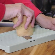Colocar sobre la tabla de picar la mandolina y rebanar la papa en rebanadas delgadas hasta terminar con todas.