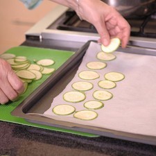 Colocar el papel encerado sobre la charola para horno y poner las rebanadas de calabacita sobre e papel, dejando un espacio entre cada rebanada.