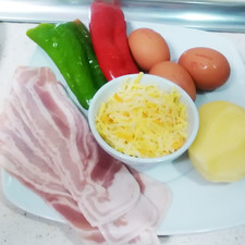 Pelamos y picamos las patatas en rodajas finas, los pimientos en tiras y cocemos los huevos.