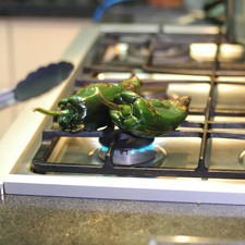 Asar los chiles poblanos directamente sobre la hornilla de la estufa, dándoles vuelta con una pinza hasta que la piel esté tostada por todos lados.