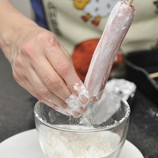 Ensartar cada salchicha en un palito de madera. Espolvorear con harina de trigo y escurrir el exceso.