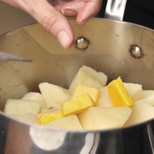 Agregar la mantequilla en trozos y machacar las papas con un machacador.