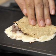 Colocar sobre cada montículo una tortilla y voltear con la pala para que el queso quede encima.