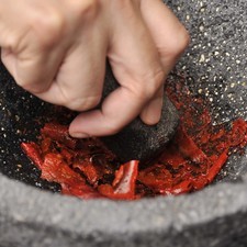 En el molcajete moler primero los chiles, agregar los ajos y la sal de mar y continuar moliendo.