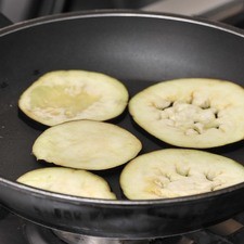 Cortar la berenjena en rodajas, espolvorear las rebanadas con sal y dejar reposando por 2 horas para quitarle el sabor amargo y desflemarla. Lavar y secar las rodajas de berenjenas y dorar en una sartén con muy poco aceite de oliva por un lado y el otro.