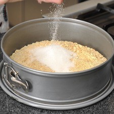 Colocar las galletas sobre el un molde desmoldable para pastel. Añadir las dos cucharadas de azúcar y mezclar.