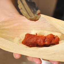 Colocar una costilla en el centro de cada tortita y envolver muy bien en forma de bola. Colocar las bolitas dentro de las hojas de maíz y envolver bien. Amarrar los dos extremos con tiritas de las mismas hojas de maíz.