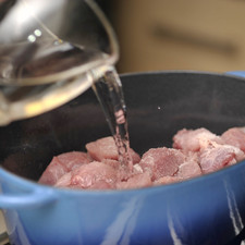 Cortar la carne de cerdo en trozos medianos de unos 5 centímetros por lado. Poner a cocer en una olla honda con la taza de agua y un poco de sal, revolver, tapar y cocer a lumbre bajita, retirando la espuma de vez en cuando y meneando.