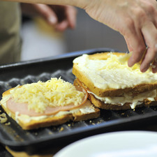 Poner la otra rebanada de pan encima con la salsa bechamel encima. Espolvorear con más queso rallado y colocar en una charola para galletas. Hornear a 400°F (200°C) hasta que el queso se vea derretido.