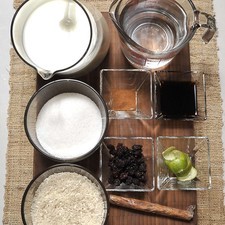 1 taza de arroz 2 tazas de agua 1 litro de leche 1 taza de azúcar 1 raja de canela 1 pizca de sal 1 cascarita de limón 4 cucharadas de esencia de vainilla Canela en polvo Pasitas