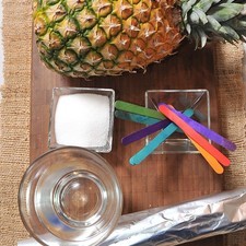 1 pieza de piña 1 taza de agua 1/4 taza de azúcar blanca papel aluminio al gusto palitos de madera al gusto