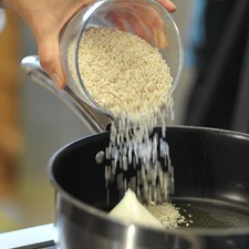 Para preparar el arroz, en una sartén verter un poco de aceite de oliva para dorar el arroz, el ajo y el cuarto de cebolla enteros, meneando con frecuencia a que quede el grano transparente (no debe quemarse).