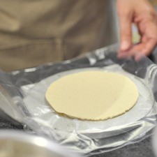 Tomar un puño de masa, colocar en la máquina tortilladora entre dos trozos de plástico, presionar para formar círculos de 11 centímetros de diámetro y 3 milímetros de espesor.