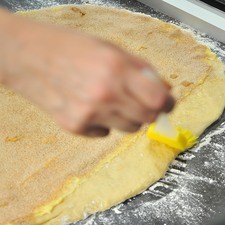 Untar la mantequilla suavizada sobre el rectángulo de masa, dejando una orilla sin untar de unos 3 centímetros en uno de los lados largos. Espolvorear uniformemente el azúcar con canela sobre la superficie enmantequillada. Aplicar un poco de agua con una brocha a la orilla que quedó sin mantequilla. S 6734 1475624055