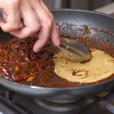 Pasar las tortillas fritas, una por una, hasta que queden bien húmedas con el mole.