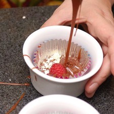 Colocar una cucharada de la mezcla dentro de cada capacillo. Agregar una cucharita de chocolate blanco rallado y una frambuesa a cada molde. Rellenar con más mezcla de chocolate. Hornear a 300°F (150°C) durante 20 minutos o hasta que la superficie esté firme al tacto.