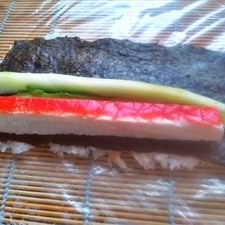 En la orilla del sushi coloca gajos de aguacate, un bastón de pepino y un surimi cortado a la mitad por lo largo, asegúrate de que a todo lo largo, el sushi tenga estos ingredientes, si es necesario coloca un pedazo más de surimi u otro ingrediente para completar, de lo contrario cuando cortes el makizushi, habrá partes que solo tengan arroz.