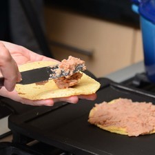 Poner a calentar 2 tortillas sobre el comal e inmediatamente untar una con los frijoles refritos.