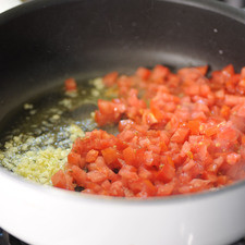 Pelar y picar las papas. Picar los jitomates en cuadros pequeños y el ajo finamente. Cortar la pechuga en trozos pequeños y reservar. Sofreír en el sartén con las dos cucharadas de aceite el ajo picado y los jitomates.