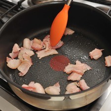 Cortar el tocino en trozos pequeños. Picar finamente el ajo y la cebolla. Cortar los pimientos en cubos pequeños, eliminando las venas blancas y las semillas. Cortar la pechuga de pollo en cubos pequeños tamaño bocado. Pelar los chícharos. Colocar la sartén sobre fuego medio y cocer los trozos de tocino aproximadamente 3 minutos hasta que se empiecen a dorar.
