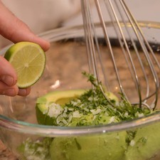 Agregar el jugo de un limón. La cebolla, el ajo y la mitad del cilantro finamente picados. Cortar el chile serrano en dos, retirar las semillas para que no pique tanto y picar finamente. Agregarlo al tazón. Sazonar con sal y pimienta y unas gotas de aceite de oliva. Machacar todo con un globo.